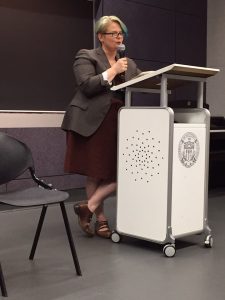 Sara Ryan behind a podium holding a microphone